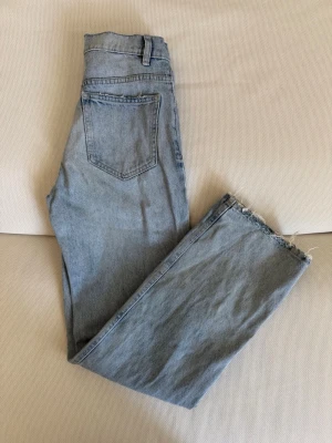 Ljusblå raka jeans med rå kant - Ljusblå jeans med rak passform och hög midja. Jeansen har klassiska fem fickor och rå, fransad kant nedtill på benen för en trendig look. Perfekta för dig som gillar en avslappnad och stilren vibe.