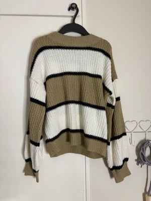 Randig stickad tröja i beige och vitt - Stickad tröja med breda ränder i beige och vitt samt smala svarta ränder. Oversized passform med långa ärmar och ribbade muddar. Perfekt för lager-på-lager och chill dagar. Materialet är grovstickat och mjukt. Inte säker på storleken men skulle säga oversized small