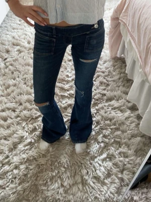Mörkblå bootcut jeans med slitningar från Gina tricot 14+💓 - mörkblå bootcut jeans med slitningar på knäna och lätt utsvängda ben. Jeansen har låg midja och är i storlek xs. Jag är cirka 159 lång och dem är någon centimeter för långa för mig💓💓 dem har en liten fläck på knät men den syns knappt💓