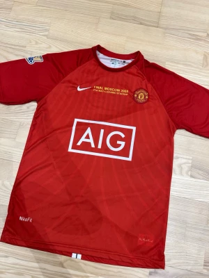 Manchester United finaltröja 2008 - Röd Manchester United matchtröja från Nike, Final Moscow 2008 edition med AIG som sponsor. Broderat klubbmärke, Nike-logga och text om finalen på bröstet. Korta ärmar och rund hals. Tillverkad i lätt och ventilerande material.