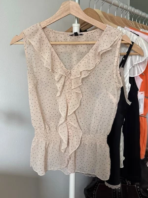 Prickig blus  - Så fin prickig beige blus med volanger och smock i midjan. Har ett litet hål spm syns på sista bilden 