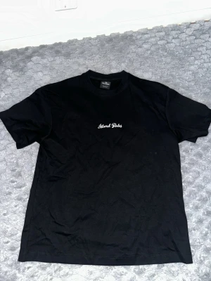 Svart t-shirt från Pull&Bear - Svart t-shirt från Pull&Bear med vit broderad text 'Street Goals' på bröstet. Klassisk rund halsringning och korta ärmar. Tillverkad i mjuk bomull för en bekväm känsla. Perfekt till jeans eller shorts för en enkel och clean look.