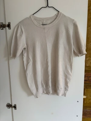 Vit stickad topp med kort ärm - En enkel och stilren Vit stickad topp med rund hals och korta ärmar. Perfekt att matcha med jeans eller kjol för en avslappnad look. Mjuk och skön mot huden.