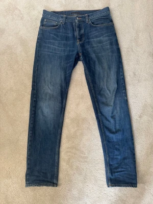 Mörkblå jeans från Nudie Jeans - Snygga mörkblå jeans från Nudie Jeans med klassisk femficksdesign och orangea sömmar. Jeansen har raka ben och subtila slitningar framtill och bak. Tillverkade i bomull med en autentisk tvättad look. Modellen är Steady Eddie II