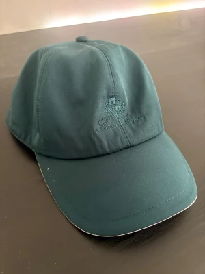 Mörkgrön keps LP - Snygg mörkgrön keps från LP med broderad logga framtill. Kepsen har klassisk böjd skärm och insida med rutigt foder samt Storm System-teknologi. Tillverkad i Italien och perfekt för dig som gillar stilrena accessoarer.