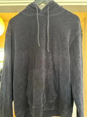 Mörkblå hoodie  - Mysig mörkblå hoodie med huva och dragsko, tillverkad i ett mjukt frottéliknande material. Klassisk känguruficka framtill och ribbade muddar vid ärmslut och nederkant. Perfekt för en avslappnad och chill stil. Knappt använd alls.