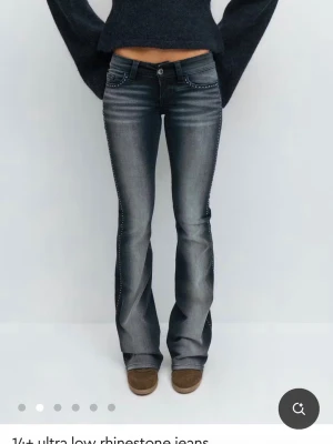 Grå utsvängda jeans med strass - Snygga grå jeans med låg midja och utsvängda ben. Jeansen har coola slitningar och är dekorerade med strass längs fickor och sidor för extra bling. Perfekta för dig som vill sticka ut och köra en trendig Y2K-look.