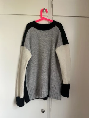 Stickad tröja i svart, grått och vitt - Säljer en stickad tröja i färgblock med svart rygg, grå framsida och vita ärmar. Tröjan är från H&M i storlek S💕