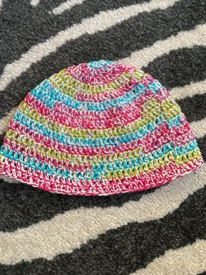 Flerfärgad virkad mössa - virkad bucket hat i rosa, blå, grön och vit. Hatten har ett randigt mönster och är gjord i bomull och akrylgarn. Sitter löst på mitt huvud som har 55cm i omkrets
