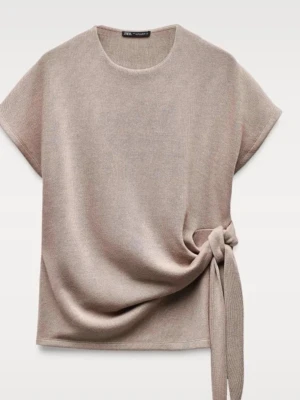 Beige stickad topp med knyt från Zara - Superfin beige stickad topp från Zara med korta ärmar och snygg knytdetalj i sidan. Toppen har en rund halsringning och är i mjukt material som känns skönt mot huden. Perfekt att styla med jeans eller kjol för en chill look.