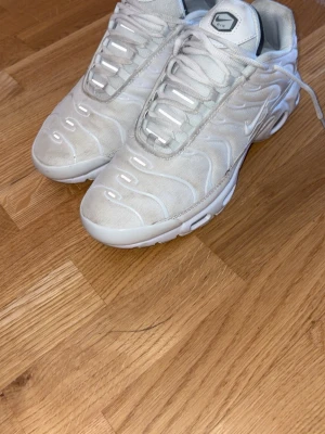 Nike vita Air Max Plus sneakers ( priset kan diskuteras)  - Säljer ett par vita Nike Air Max Plus sneakers med ikoniska vågiga detaljer och synlig dämpning i sulan. Skorna har mesh- och syntetmaterial, vita snören och diskret Swoosh på sidan. Perfekta för dig som gillar stilrena och sportiga sneakers.