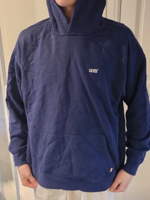 Mörkblå hoodie från Levi's - Snygg mörkblå hoodie från Levi's med klassisk huva och magficka. Diskret Levi's-logga i vitt på bröstet och relaxed fit. Tillverkad i mjukt bomullsmaterial som är skönt mot huden. Perfekt för en chill och avslappnad stil.