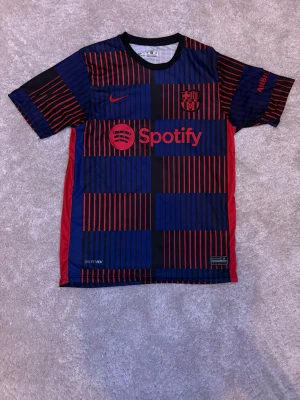Barcelona matchtröja Nike blå/röd - Snygg FC Barcelona matchtröja från Nike i blått och rött med röda detaljer och sponsorloggor från Spotify och UNHCR. Tröjan har trycket 'LAMINE YAMAL 19' på ryggen och är tillverkad i ett lätt, snabbtorkande material. Perfekt för fotbollsträning eller att bära till vardags.