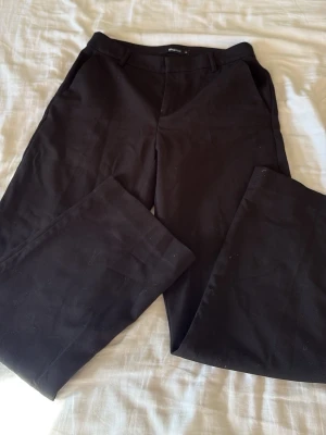 Svarta kostymbyxor Gina Tricot - Stilrena svarta kostymbyxor från Gina Tricot med raka ben och klassisk passform. Byxorna har hällor för skärp och sidofickor. Perfekta för en dressad look och enkla att matcha med olika toppar.