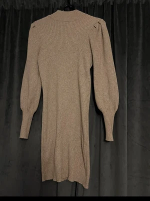 Beige ribbad stickad klänning ONLY - Beige ribbad stickad klänning från ONLY med lång ärm och puff vid axlarna. Klänningen har en rak passform och slutar ovanför knäna. Perfekt för dig som gillar en enkel men trendig look. Storlek M med jag som har S kan ha den o den sitter fint då med, den e stretchig. 