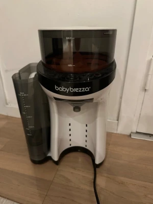 Babybrezza Formula Pro Advanced - Automatisk mjölkersättningsmaskin från Babybrezza i vitt och svart. Maskinen har tydliga vatten- och pulverbehållare samt digitala knappar på framsidan. Perfekt för att snabbt blanda ersättning till bebisar. Originalkartong medföljer.