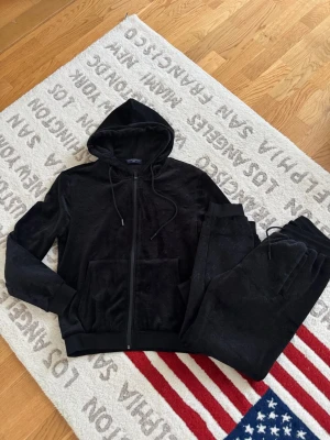 Svart velour loungewear-set Louis Vuitton - Säljer ett svart loungewear-set i mjuk velour från Louis Vuitton. Setet består av en hoodie med dragkedja och fickor samt matchande byxor med resår och dragsko i midjan. Båda plaggen har det klassiska LV-monogrammet i materialet.