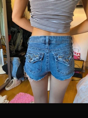 Y2k jeansshorts - Säljer ett par blå jeansshorts med låg midja. Shortsen har snygga detaljer med pärlor och broderi på bakfickorna. Skriv gärna vid frågor💕
