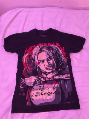 Svart t-shirt Black Timber tryck (Harley quinn) - Till alla Harley quinn fans! Cool svart t-shirt från Black Timber med färgstarkt tryck framtill som föreställer två tecknade figurer och texten 'Daddy's Lil Monster'. T-shirten har korta ärmar och rund hals. Perfekt för dig som gillar grafiska motiv och streetstyle.