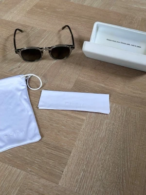 Grå CHIMI solglasögon  - Snygga solglasögon från CHIMI med transparent grå båge och runda, mörka glas. Kommer med originalväska, putsduk och hårt fodral. Perfekta för dig som vill ha en stilren och modern look i sommar.