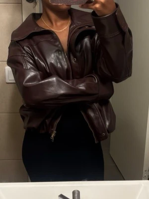 Mörkbrun oversized skinnjacka - Snygg mörkbrun skinnjacka med oversized passform och bred krage. Jackan har dragkedja framtill och tryckknappar, samt långa ärmar. Perfekt för dig som vill ha en trendig och stilren look.