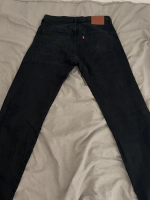 Svarta Levi's jeans med raka ben - Säljer ett par svarta jeans från Levi's med klassisk femficksdesign och raka ben. Jeansen har en brun läderpatch bak i midjan och den ikoniska röda Levi's-taggen på ena bakfickan. Perfekta för en stilren och avslappnad look.