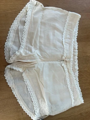 Vita spetskantade shorts med fickor - Säljer ett par vita shorts med elastisk midja och dekorativa spetskanter runt ben och midja. Shortsen har två fickor bak och fina broderidetaljer. Tillverkade i ett tunt, mjukt tyg som känns luftigt och bekvämt. Perfekta för en avslappnad och söt stil. Ett par kostar 250, men säljer även dom tillsammans för 500 då dom var köpte för 1000kr var i butik.