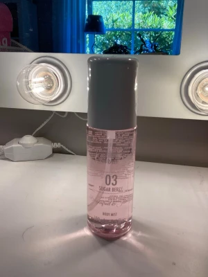 Sugar Berry Body Mist 03 - Fräsch body mist med doften Sugar Berry i en cylinderformad plastflaska. Flaskan är genomskinlig med ljusrosa vätska och har en vit spraykork och lock. Volymen är 100 ml och designen är enkel och modern, perfekt för dig som gillar söta och bäriga dofter. Dump av sol de Janeiro 68✨💗