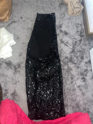 Svart glittrig paljettklänning - Säljer en svart, glittrig klänning täckt med paljetter. Klänningen är ärmlös och har en kroppsnära passform som ger en snygg siluett. Perfekt för dig som vill sticka ut och glänsa på nästa fest! Materialet känns mjukt och följsamt.