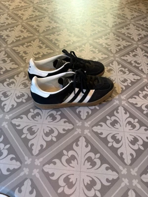 Adidas Samba svartvita sneakers - Klassiska Adidas Samba sneakers i svart mocka med vita läderdetaljer och de ikoniska tre ränderna på sidan. Skorna har gummisula och svart snörning. Perfekta för en sportig och stilren look. Orginal box finns