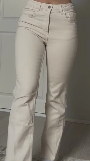 Beiga raka jeans från Zara - Säljer ett par snygga beiga jeans från Zara med rak passform och hög midja. Jeansen har klassisk femficksdesign, bälteshällor och stängs med knapp och dragkedja. Perfekta till en avslappnad och trendig look.