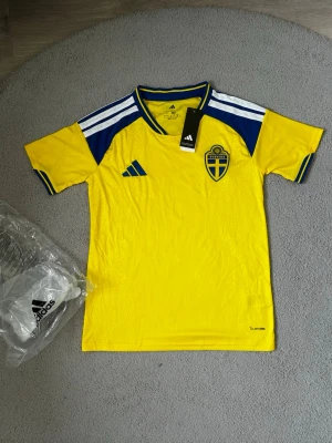 Svensk landslagströja Adidas gul - Säljer en gul svensk landslagströja från Adidas med blå detaljer och vita ränder på axlarna. Tröjan har broderat Sverige-emblem på bröstet och Adidas-logga. Tillverkad i lätt och funktionellt material.Den är i bästa kvalité och helt ny, därför är den 10 av 10 i skick.Väldigt fin och bra för sommaren och för träningen. Fraktar så fort du har köpt🚚📦Aktiv 24/7✅ Hör av dig via frågor⁉️