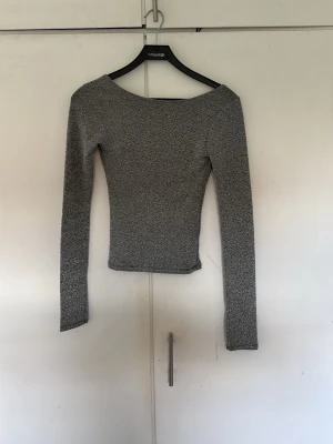 Glittrig långärmad topp med öppen rygg - Snygg långärmad topp i glittrigt silvermaterial med en djup, öppen rygg. Tight passform och rundad halsringning framtill. Perfekt för dig som vill sticka ut lite extra med en trendig och elegant look.