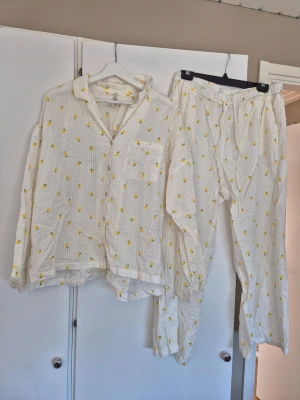 Bäckebölja pyjamas set Lindex stl M - Supermysig vit pyjamas från Lindex med sött citrongult mönster. Setet består av en långärmad skjorta med bröstficka och matchande byxor med resår i midjan. Materialet är mjukt och luftigt, perfekt för chillkvällar hemma. Fått sig mindre fläckar, men är väldigt härligt tyg och har väldigt mycket kvar att ge!☀️☀️