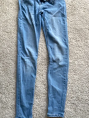 Ljusblå skinny jeans från 157 - Säljer ett par ljusblå skinny jeans från 157 med klassiska fem fickor och gul kontrastsöm. Jeansen har normal midja och är tillverkade i mjuk denim med lite stretch för skön passform. Perfekta till en avslappnad look.