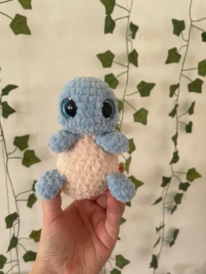 Virkad Squirtle - Supergulligt handvirkat Squirtle-gosedjur med ljusblå kropp, beige mage och brun skal. Tillverkad i mjukt garn med stora blanka ögon. Perfekt som dekoration eller present till Pokémon-fans.