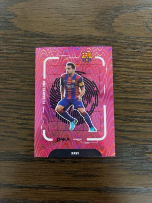 FC Barcelona Xavi 18/99 - Unikt samlarkort med Xavi i FC Barcelonas matchställ. Kortet har en färgstark, röd-rosa bakgrund med klubbens logga och texten 'LOCKED' på baksidan. Begränsad upplaga, numrerat 18/99. Perfekt för fotbollsfans och samlare.