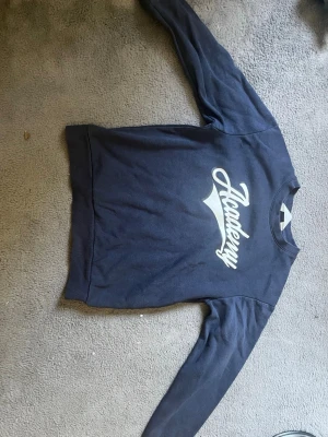 Mörkblå sweatshirt från H&M - Mörkblå sweatshirt från H&M med trycket 'Academy' i vitt framtill. Tröjan har rund halsringning och långa ärmar. Perfekt för en avslappnad och sportig stil. Tillverkad i mjukt bomullsmaterial. Och en låg profil look. Vid frågor är de bara att skriva pris kan diskuteras 