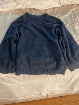 Mörkblå fluffig stickad tröja - Mysig mörkblå stickad tröja med fluffig textur och rund hals. Tröjan har långa ärmar och ribbade muddar vid ärmslut och nederkant. Perfekt för kyliga dagar och enkel att matcha med jeans eller kjol.