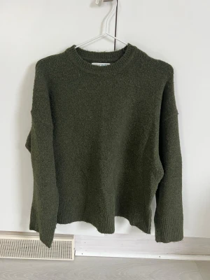 Mörkgrön stickad tröja Primark XS - Mysig mörkgrön stickad tröja från Primark med rund halsringning och långa ärmar. Tröjan har ribbstickade muddar vid ärmslut och nederkant, perfekt för kyliga dagar. Enkel och stilren design som passar till det mesta.