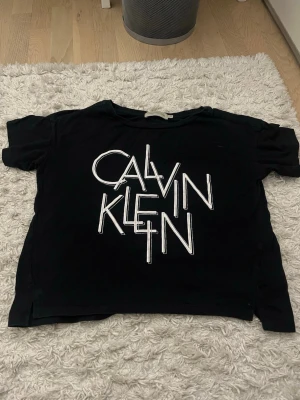 Svart Calvin Klein Jeans t-shirt - Säljer en svart t-shirt från Calvin Klein Jeans med stort vitt grafiskt tryck på framsidan. T-shirten har rund halsringning och korta ärmar. Perfekt för dig som gillar streetwear och vill ha en statement-piece i garderoben.