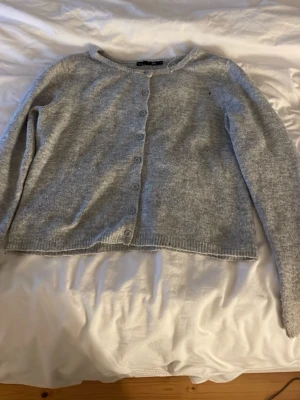 Ljusgrå kofta från Polo lager 157 - Mysig ljusgrå kofta från lager157 med rund halsringning och knappar framtill. Och ett litet hål men inget man lägger märke till. Tillverkad i mjukt stickat material och har långa ärmar samt ribbade muddar.