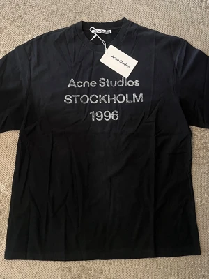 Svart Acne Studios t-shirt - Snygg svart t-shirt från Acne Studios med trycket 'Acne Studios STOCKHOLM 1996' i vitt på bröstet. Klassisk passform och rund hals. Perfekt för dig som gillar minimalistisk och stilren design.
