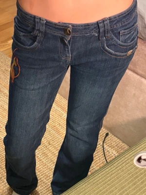 Mörkblå jeans med brodyr från Pepe Jeans🌸 - Säljer ett par mörkblå jeans från Pepe Jeans med färgglada broderier på fickorna och en klassisk femficksmodell. Jeansen har raka ben och kontrastsömmar som ger en snygg detalj. 