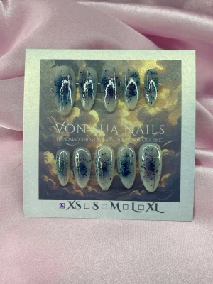 NocturneInk (XS);Medium Almond - Unika handgjorda press-on naglar i en medium mandelform. Basen är milky white med mörk blått och mermaid glitter samt silver abstrakta detaljer. Perfekt för dig som vill ha något kreativt och konstnärligt på naglarna. Material: gelé.