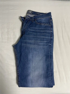 Blå jeans med tvättade detaljer - Säljer ett par blå jeans med snygga tvättade detaljer och klassisk femficksdesign. Jeansen har rak passform och är tillverkade i denim med stretch för extra komfort. Perfekta för dig som gillar en avslappnad och stilren look.