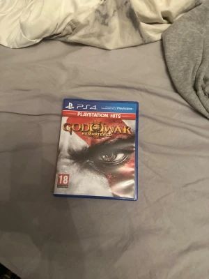 God of War Remastered PS4 spel - Säljer God of War Remastered till PS4 från PlayStation Hits-serien. Omslaget är i svart, vitt och rött med Kratos ikoniska öga i fokus. Spelet är i fysisk utgåva med blå plastfodral och PEGI 18-märkning. Perfekt för dig som gillar action och äventyr.