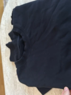 Svart sweatshirt från ARKET - En stilren svart sweatshirt från ARKET i mjukt bomullsmaterial. Klassisk rund halsringning och enkel design utan tryck eller detaljer. Perfekt för en clean och avslappnad look. Tillverkad i 100% bomull.