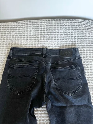 Svarta Lee jeans - Säljer ett par svarta Lee Jessica jeans med klassisk femficksdesign och raka bakfickor. Jeansen har en snygg tvättad finish. Perfekta för dig som gillar en stilren och tidlös look. Strl 28/33❣️