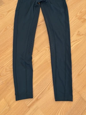 Svarta ridleggings från Horze - Snygga svarta tunna ridleggings från Horze med diskreta greppdetaljer längs benen. Tillverkade i stretchigt material med polyester och elastan för en bekväm och följsam passform. Perfekta för dig som vill ha både stil och komfort. 